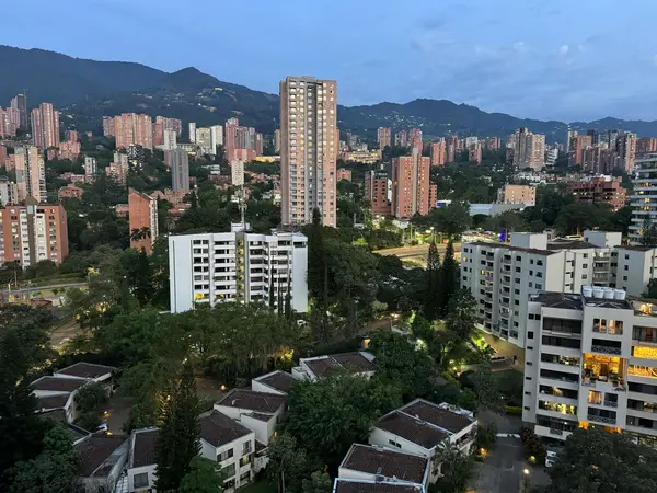 View of Medellín's Aburrá valley at dusk with brick apartment towers stacked up green hillsides and lights coming on across the city